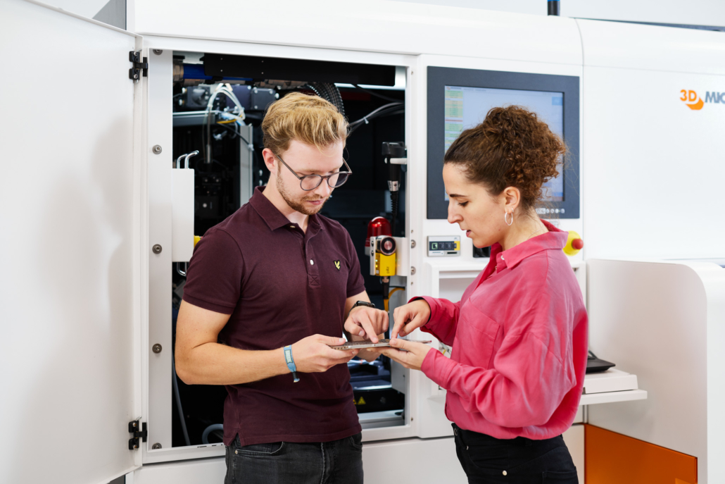 Eine Ingenieurin erklärt einem Schüler die Materialbearbeitung an einer modernen Lasermaschine.